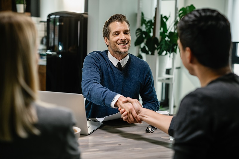 Happy financial advisor shaking hands with a couple.